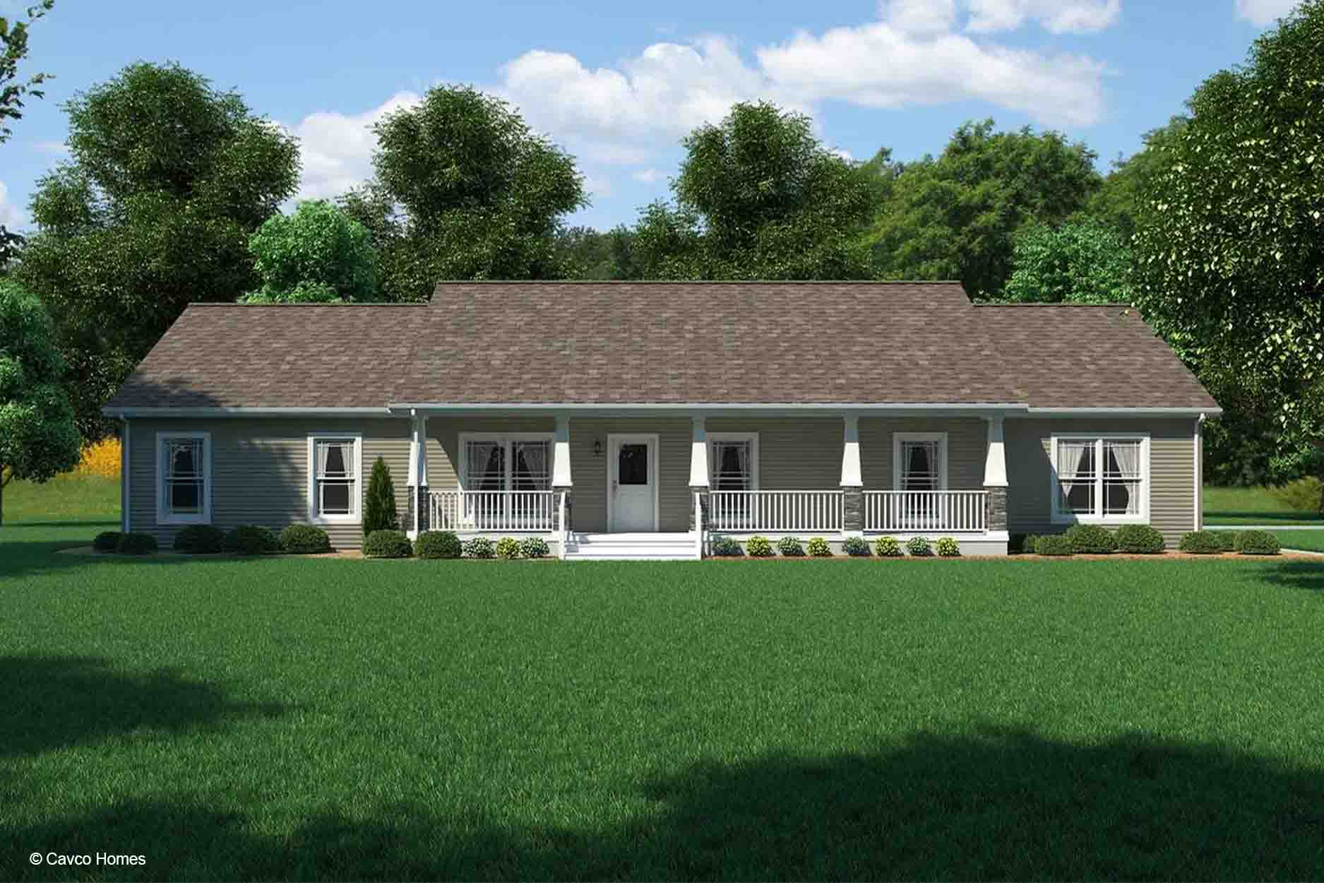 Single-story modular home with a large front porch, surrounded by trees and a green lawn, under a blue sky.