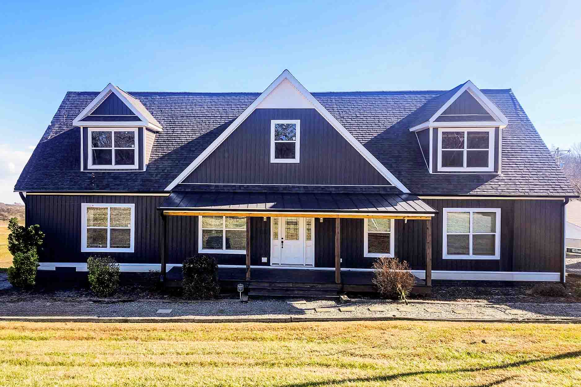 A modern black modular home with white trim, a steep roof, and multiple windows, set on a sunny lawn.
