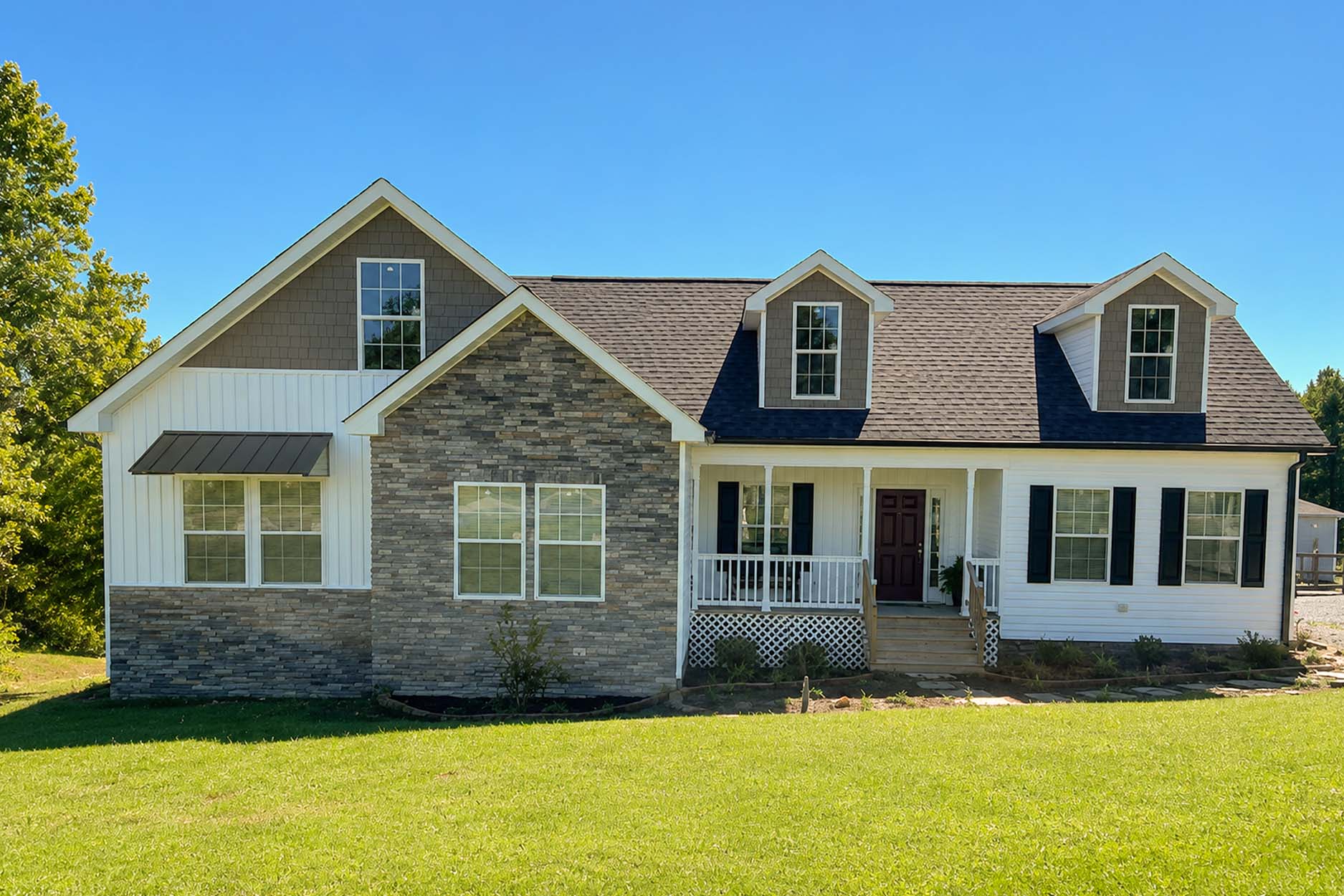 Modern modular home with stone and siding exterior, front porch, and dormer windows on a sunny day.
